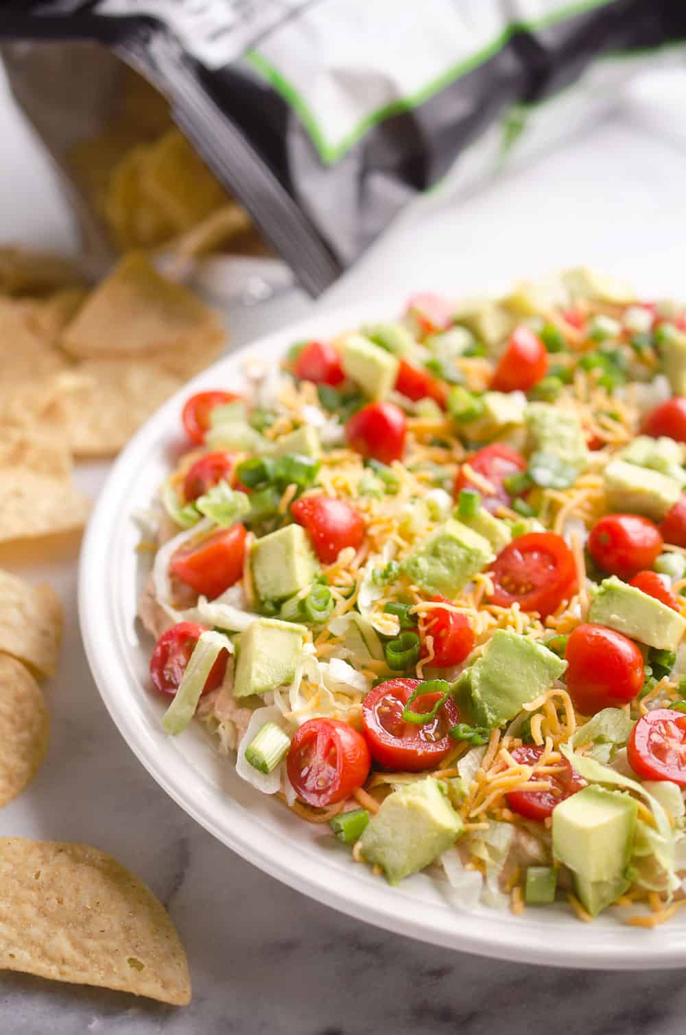 Skinny Taco Dip is a light and zesty appetizer that is a serious crowd-pleaser! This easy snack is lightened up with Greek yogurt, salsa and light cream cheese and topped with healthy avocado, tomatoes and green onions! Serve with your favorite chips for a treat everyone will love.