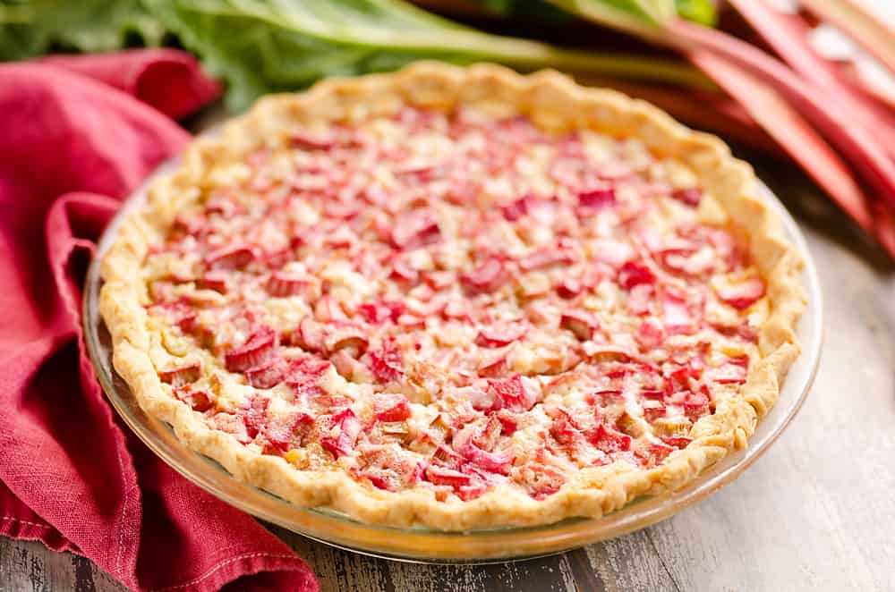 Rhubarb Custard Pie on table with stalks of rhubarb