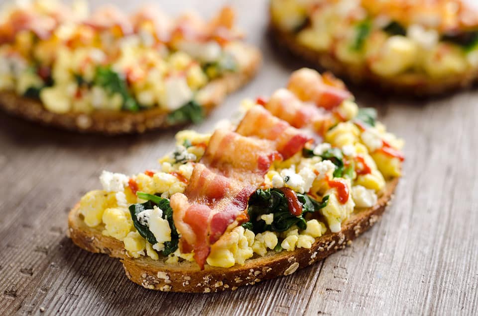 Sriracha Bacon Bleu Cheese Breakfast Toasts are a light meal bursting with bold and spicy flavors. Fluffy scrambled eggs and spinach are piled on whole wheat toast and topped with a slice of bacon, bleu cheese crumbles and sriracha for a breakfast you won't soon forget!