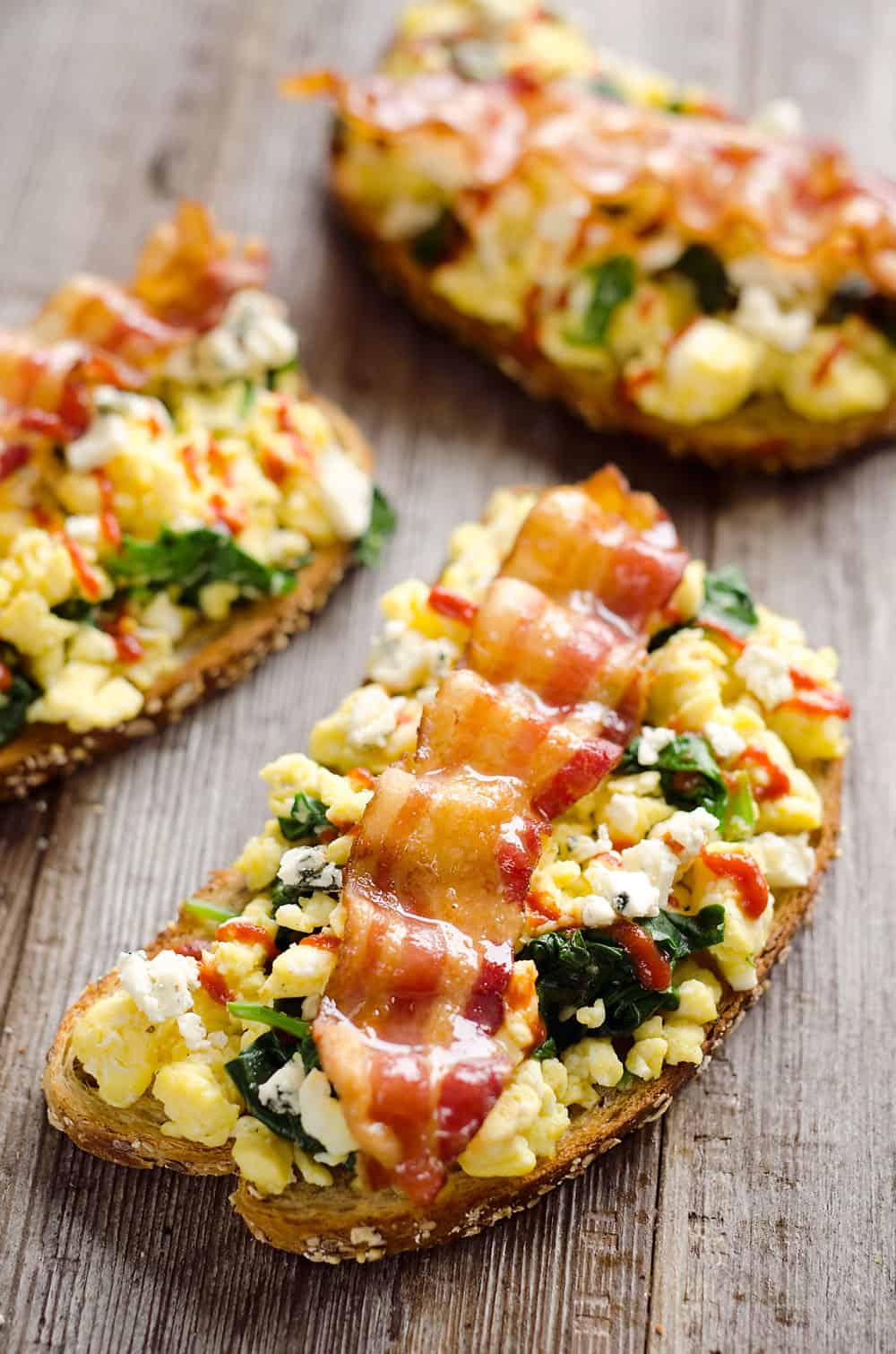 Sriracha Bacon Bleu Cheese Breakfast Toasts are a light meal bursting with bold and spicy flavors. Fluffy scrambled eggs and spinach are piled on whole wheat toast and topped with a slice of bacon, bleu cheese crumbles and sriracha for a breakfast you won't soon forget!