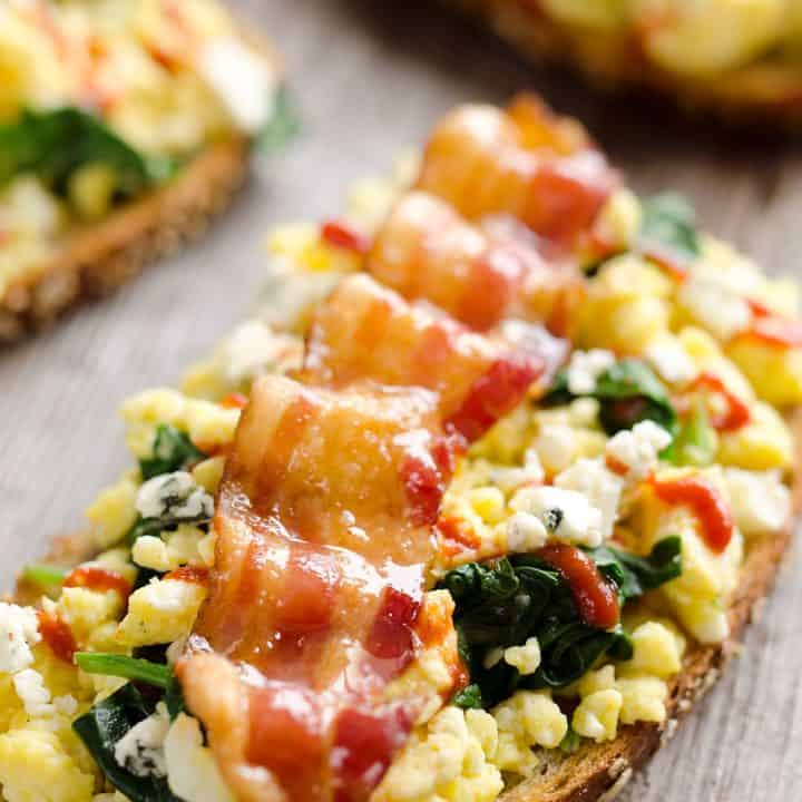Sriracha Bacon Bleu Cheese Breakfast Toasts are a light meal bursting with bold and spicy flavors. Fluffy scrambled eggs and spinach are piled on whole wheat toast and topped with a slice of bacon, bleu cheese crumbles and sriracha for a breakfast you won't soon forget!