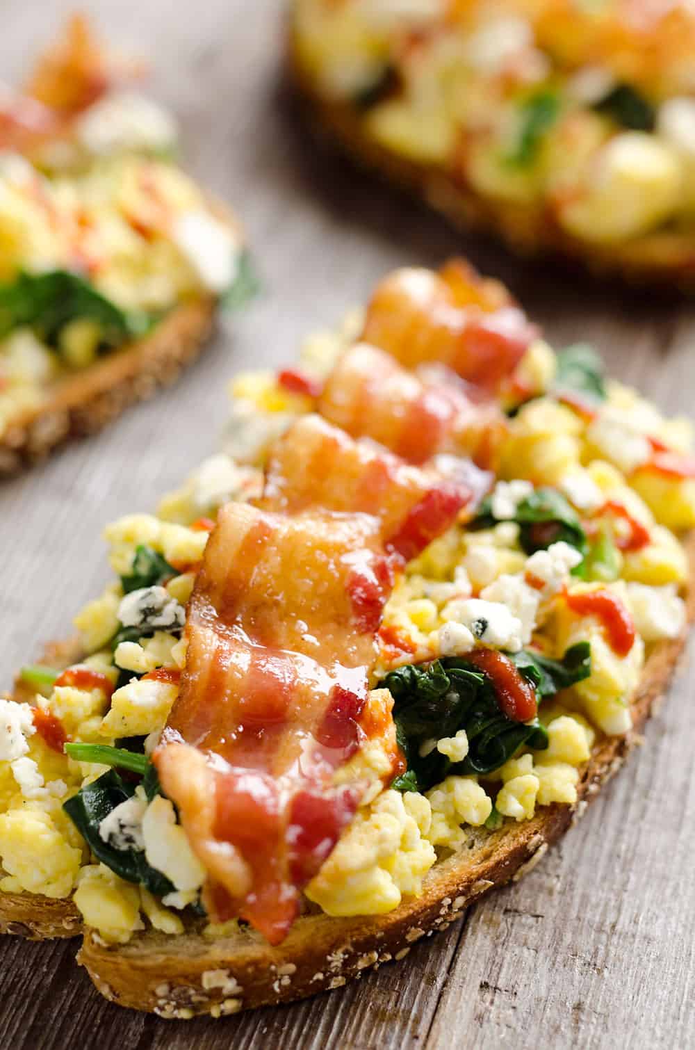 Sriracha Bacon Bleu Cheese Breakfast Toasts are a light meal bursting with bold and spicy flavors. Fluffy scrambled eggs and spinach are piled on whole wheat toast and topped with a slice of bacon, bleu cheese crumbles and sriracha for a breakfast you won't soon forget!