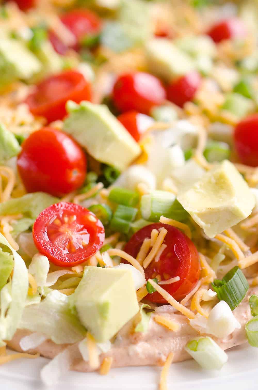 Skinny Taco Dip is a light and zesty appetizer that is a serious crowd-pleaser! This easy snack is lightened up with Greek yogurt, salsa and light cream cheese and topped with healthy avocado, tomatoes and green onions! Serve with your favorite chips for a treat everyone will love.