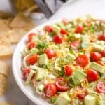 Skinny Taco Dip is a light and zesty appetizer that is a serious crowd-pleaser! This easy snack is lightened up with Greek yogurt, salsa and light cream cheese and topped with healthy avocado, tomatoes and green onions! Serve with your favorite chips for a treat everyone will love.