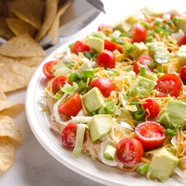 Skinny Taco Dip is a light and zesty appetizer that is a serious crowd-pleaser! This easy snack is lightened up with Greek yogurt, salsa and light cream cheese and topped with healthy avocado, tomatoes and green onions! Serve with your favorite chips for a treat everyone will love.