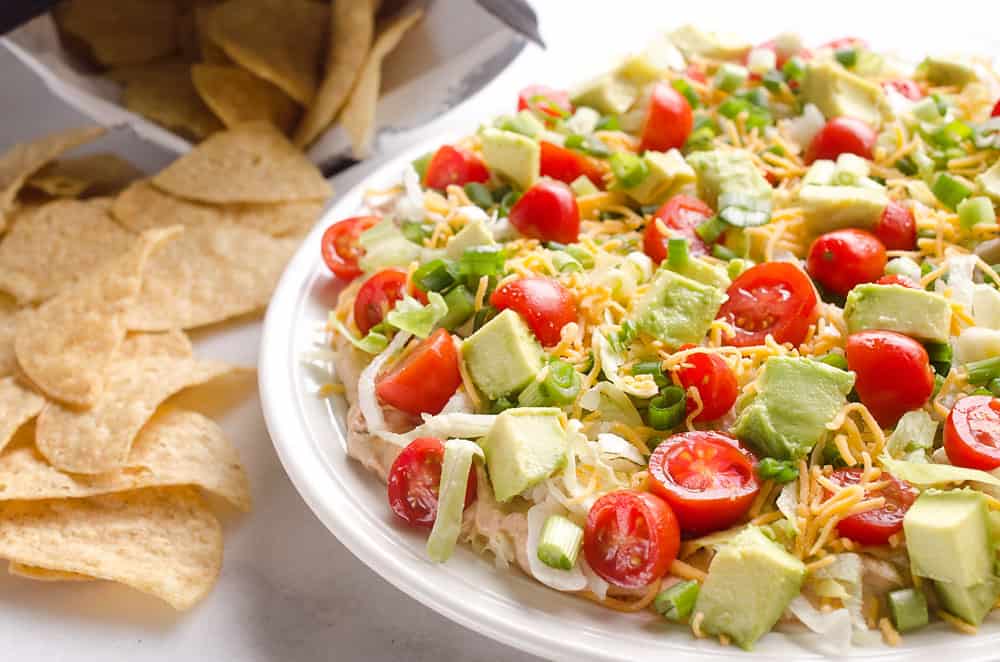 Skinny Taco Dip is a light and zesty appetizer that is a serious crowd-pleaser! This easy snack is lightened up with Greek yogurt, salsa and light cream cheese and topped with healthy avocado, tomatoes and green onions! Serve with your favorite chips for a treat everyone will love.