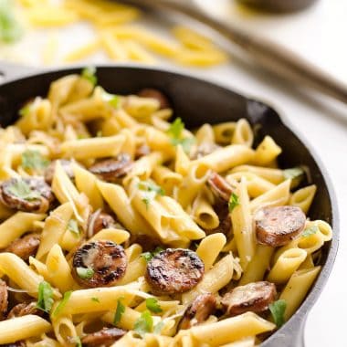 cast iron skillet with penne pasta and chicken apple sausage on table with spoon