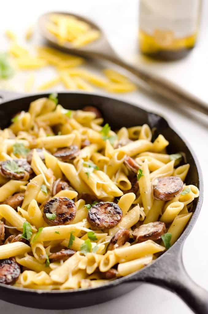 cast iron skillet with penne pasta and chicken apple sausage on table with spoon