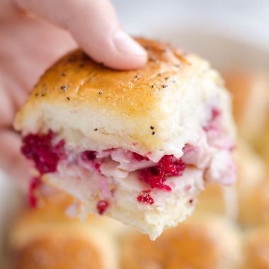 Cheesy Cranberry Turkey Baked Sliders held in hand over pan