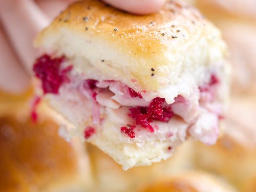 Cheesy Cranberry Turkey Baked Sliders held in hand over baking pan