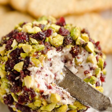 Cranberry Pistachio Cheese Ball is a festive red and green appetizer fantastic for the holidays! A cream cheese and cranberry mixture is rolled in salty pistachios and served with your favorite crackers for the perfect party food.