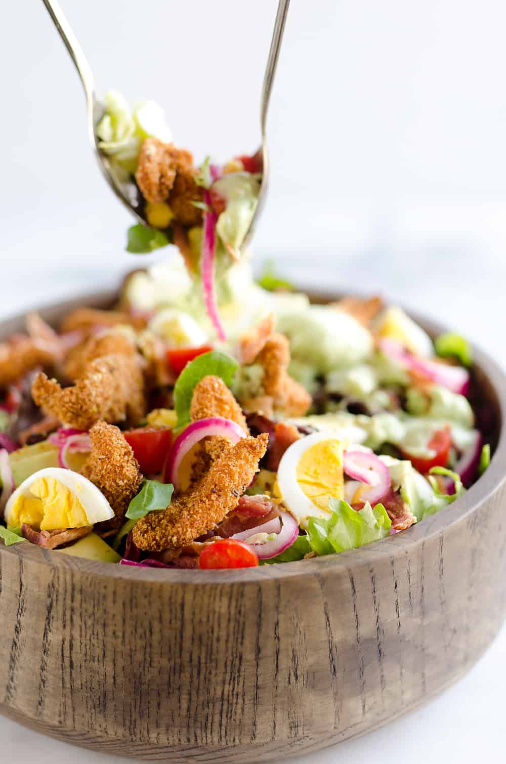 Crispy Chicken & Avocado Cobb Salad is an easy 20 minute salad recipe made in your Airfryer with Gold'n Plump Chipotle Adobo SHAKERS, bacon, veggies, lightly pickled onions and a creamy Avocado Lime Green Goddess Sauce. This hearty salad is a healthy dinner idea bursting with bold flavor and crunch!