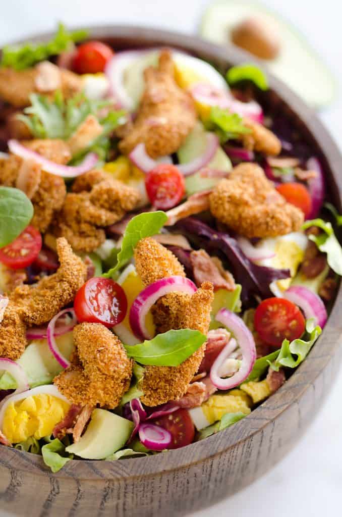 Crispy Chicken & Avocado Cobb Salad is an easy 20 minute salad recipe made in your Airfryer with Gold'n Plump Chipotle Adobo SHAKERS, bacon, veggies, lightly pickled onions and a creamy Avocado Lime Green Goddess Sauce. This hearty salad is a healthy dinner idea bursting with bold flavor and crunch!