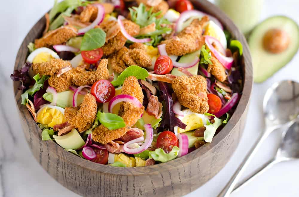 Crispy Chicken & Avocado Cobb Salad is an easy 20 minute salad recipe made in your Airfryer with Gold'n Plump Chipotle Adobo SHAKERS, bacon, veggies, lightly pickled onions and a creamy Avocado Lime Green Goddess Sauce. This hearty salad is a healthy dinner idea bursting with bold flavor and crunch!