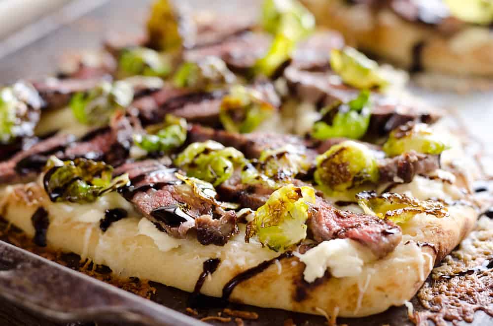 Steak, Goat Cheese & Roasted Brussels Sprout Flatbread is a hearty dinner idea bursting with bold flavors. A chewy naan bread is topped with goat cheese, grilled steak, roasted brussels sprout leaves and a balsamic glaze for a delicious and unique recipe you will make again and again!