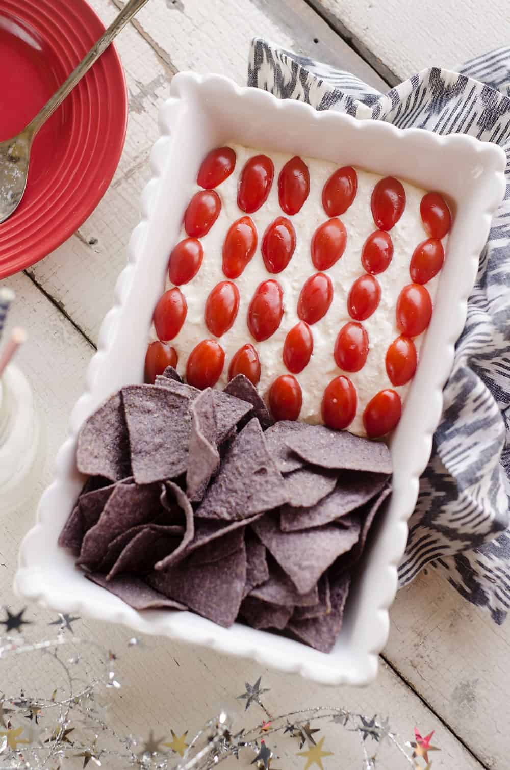 Patriotic Flag Parmesan Garlic Chip Dip is a festive appetizer recipe perfect for a holiday party with red, white and blue colors! A creamy Parmesan garlic dip is topped with cherry tomatoes and served with blue corn tortilla chips for a delicious dish sure to be a crowd pleaser. 