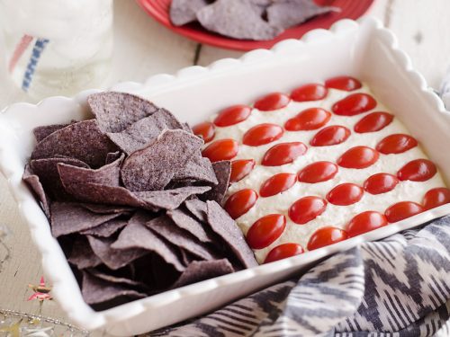 Patriotic Flag Parmesan Garlic Chip Dip is a festive appetizer recipe perfect for a holiday party with red, white and blue colors! A creamy Parmesan garlic dip is topped with cherry tomatoes and served with blue corn tortilla chips for a delicious dish sure to be a crowd pleaser. 