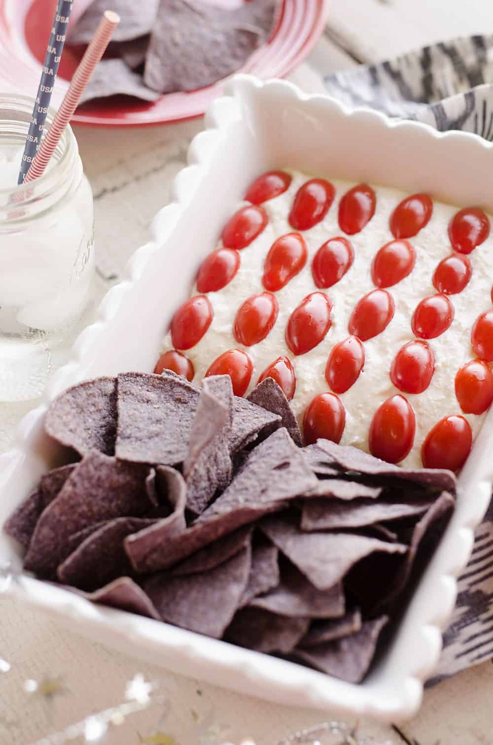 Patriotic Flag Parmesan Garlic Chip Dip is a festive appetizer recipe perfect for a holiday party with red, white and blue colors! A creamy Parmesan garlic dip is topped with cherry tomatoes and served with blue corn tortilla chips for a delicious dish sure to be a crowd pleaser. 