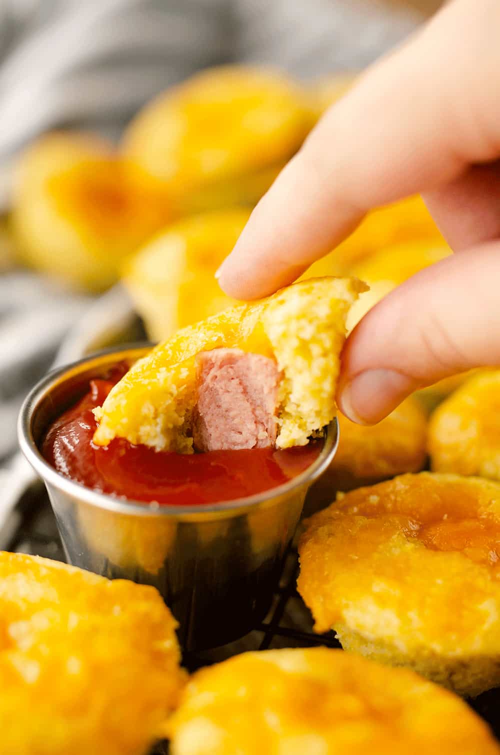 Cheesy Green Chili Mini Corn Dog Muffins dipping in ketchup