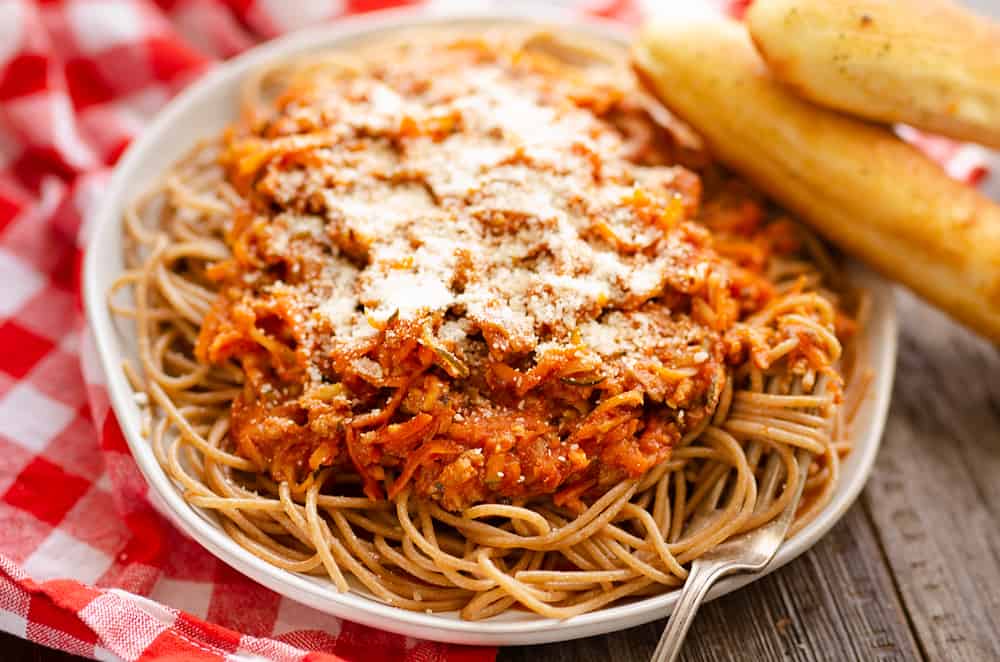 whole wheat spaghetti and vegetables served with breadsticks