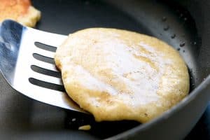 protein pancake being cooked in skillet with spatula