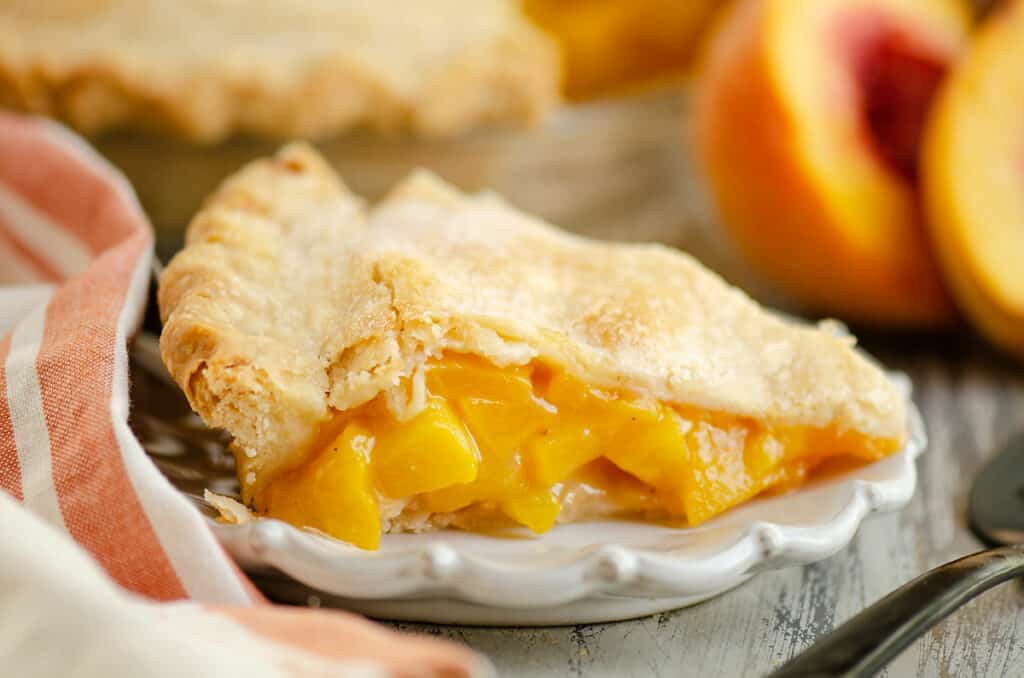 slice of peach pie on plate with peaches
