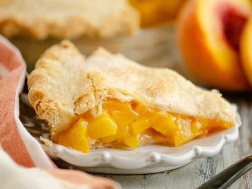 slice of peach pie on plate with peaches