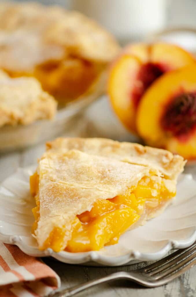 slice of peach pie on plate next to peaches