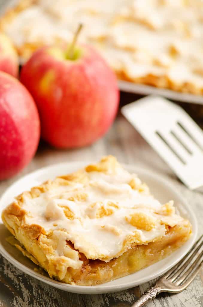 Glazed Apple Pie Bar on plate sitting on table with apples