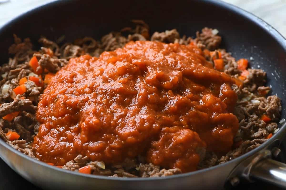 pasta sauce over hamburger and veggie mix in skillet