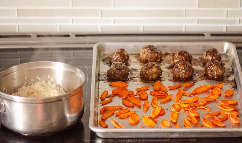 Glazed Hoisin Meatballs and roasted carrots on sheet pan and rice in pot on stove