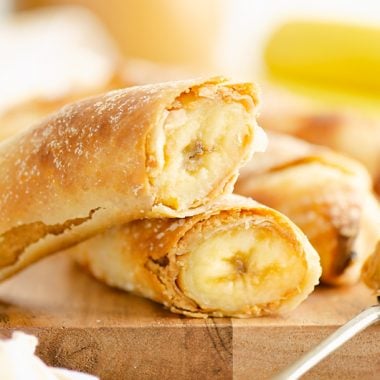 Air Fryer Peanut Butter Banana Egg Rolls on cutting board with spoonful of peanut butter