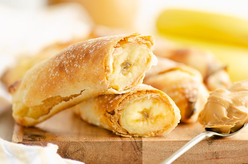 Air Fryer Peanut Butter Banana Egg Rolls on cutting board with spoonful of peanut butter