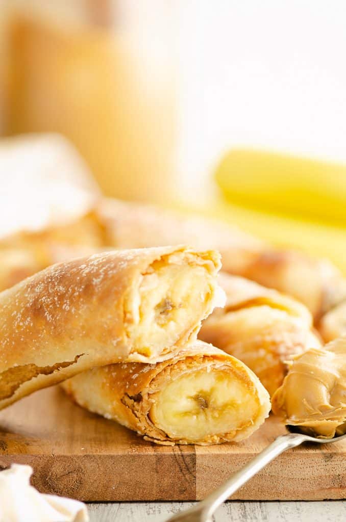 Peanut Butter Banana Egg Rolls on cutting board with spoonful of peanut butter and bananas
