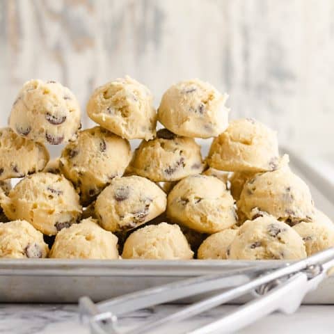 Frozen Chocolate Chip Cookie Dough Pucks stacked on cookie sheet with cookie scooper