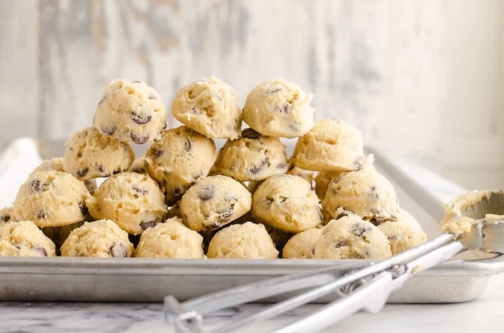 Frozen Chocolate Chip Cookie Dough Pucks stacked on cookie sheet with cookie scooper