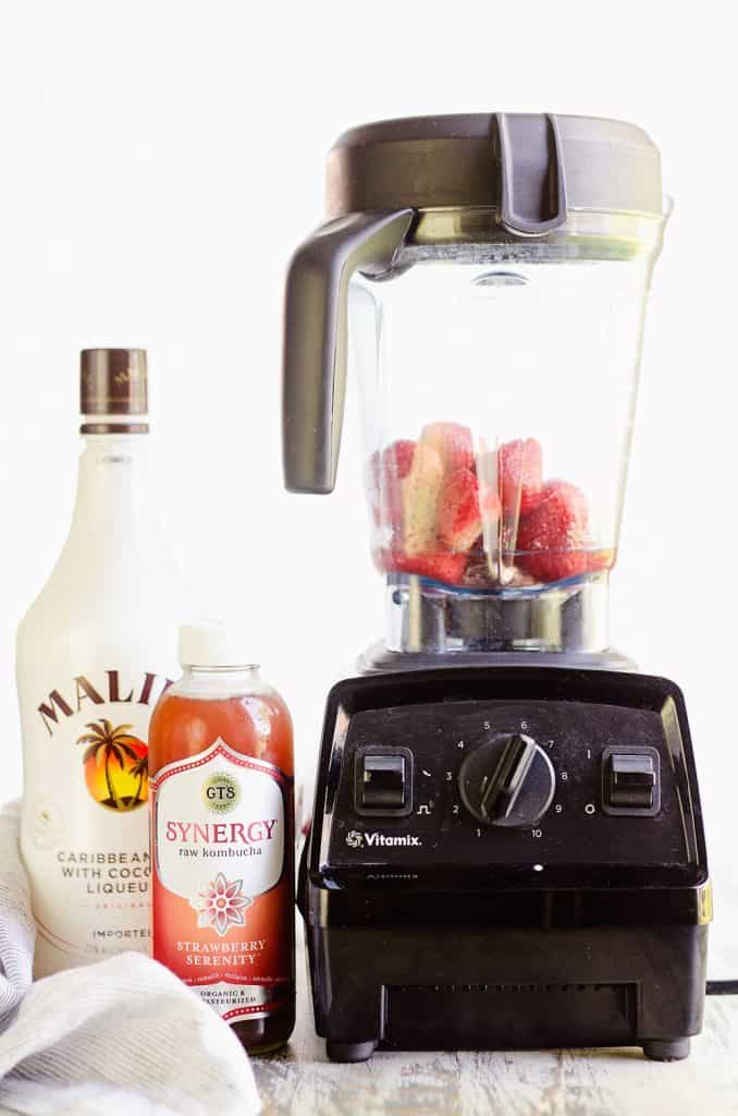 Frozen Strawberries in blender next to kombucha and Malibu rum