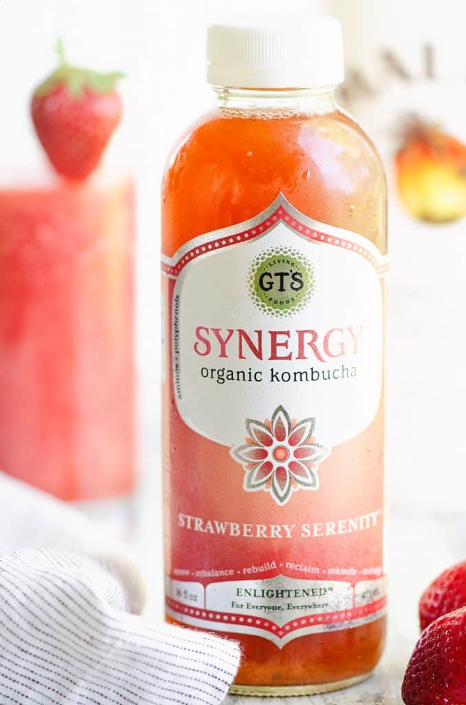 GTs Synergy Strawberry Kombucha bottle on table with cocktail and strawberries