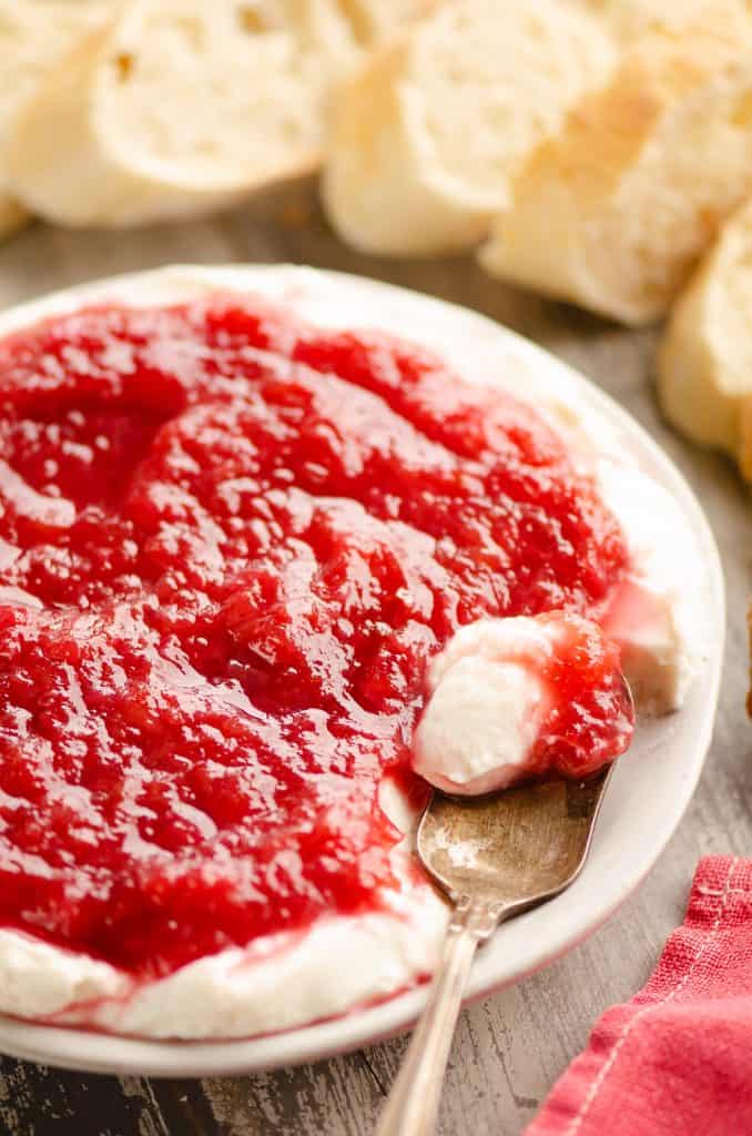 Whipped goat cheese topped with a rhubarb sauce served on a small appetizer plate with a spoon and French bread