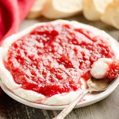 Whipped goat cheese topped with a rhubarb sauce served on a small appetizer plate with a spoon and French bread