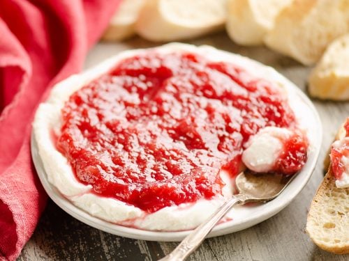 Whipped goat cheese topped with a rhubarb sauce served on a small appetizer plate with a spoon and French bread