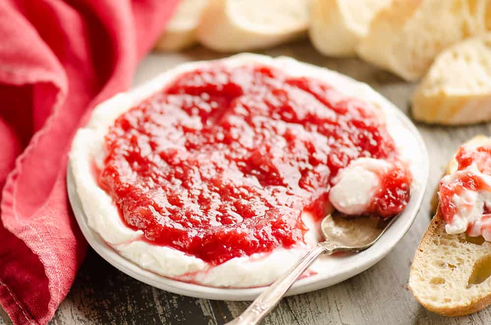 Whipped goat cheese topped with a rhubarb sauce served on a small appetizer plate with a spoon and French bread