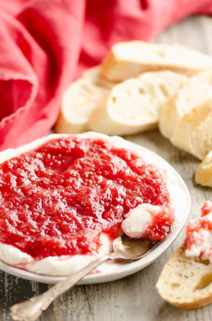 Whipped goat cheese topped with a rhubarb sauce served on a small appetizer plate with a spoon and French bread