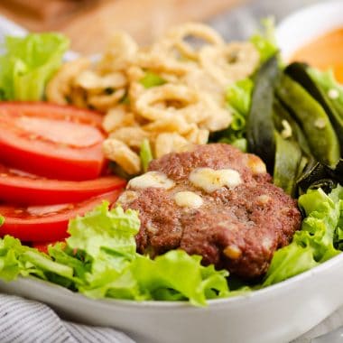 Smoked Cheese Curd Burger Salad in white bowl with side of chipotle lime southwest dressing