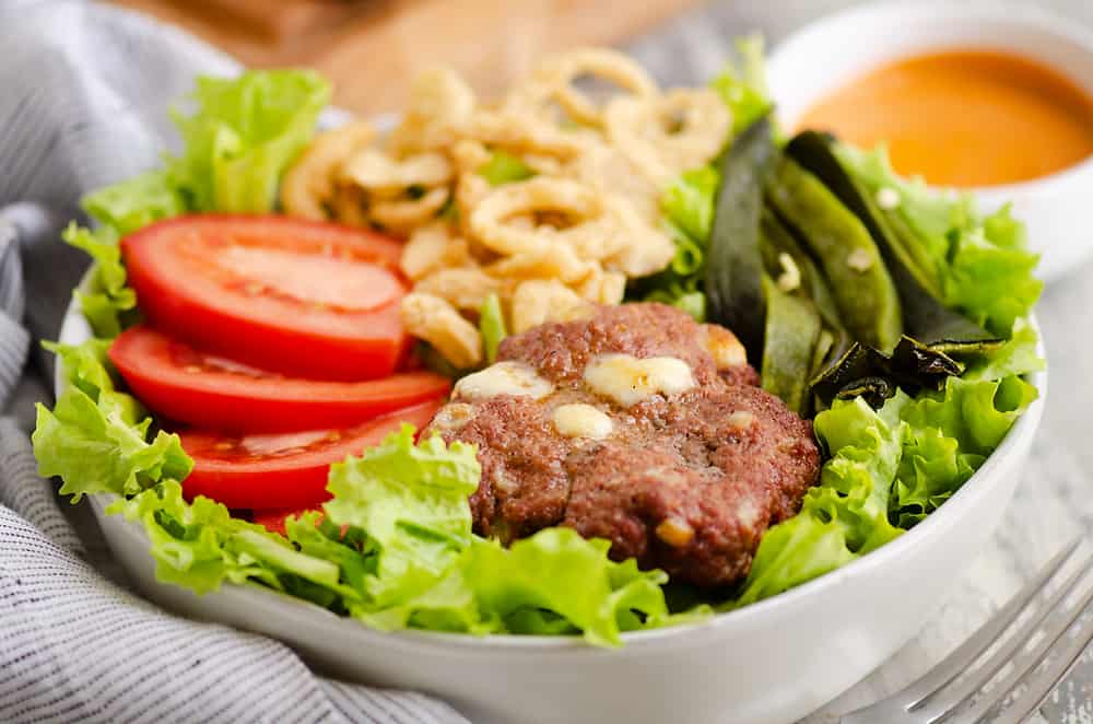 Smoked Cheese Curd Burger Salad in white bowl with side of chipotle lime southwest dressing