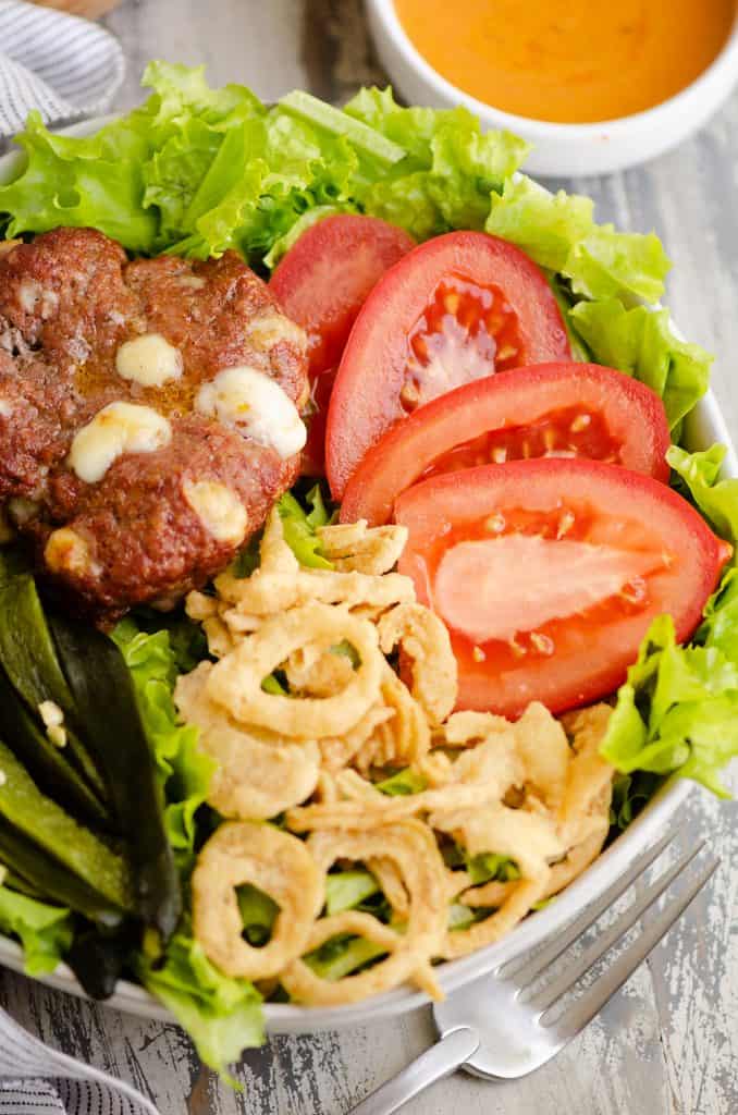 Smoked Cheese Curd Burger Salad in white bowl with side of chipotle lime southwest dressing