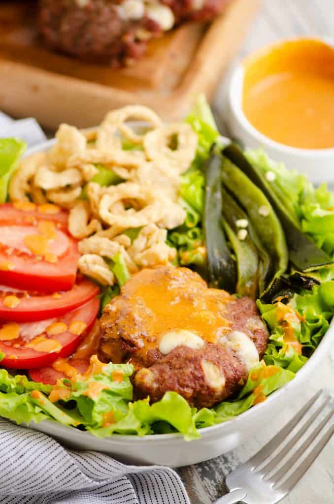 Smoked Cheese Curd Burger Salad in white bowl with side of chipotle lime southwest dressing
