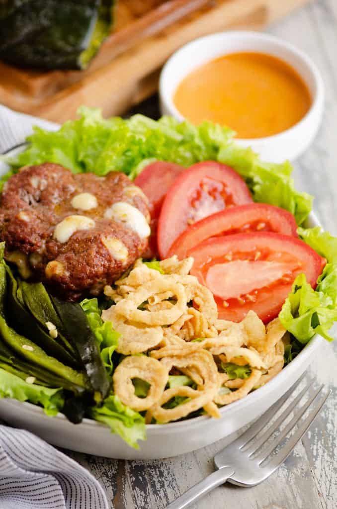 Smoked Cheese Curd Burger Salad in white bowl with side of chipotle lime southwest dressing