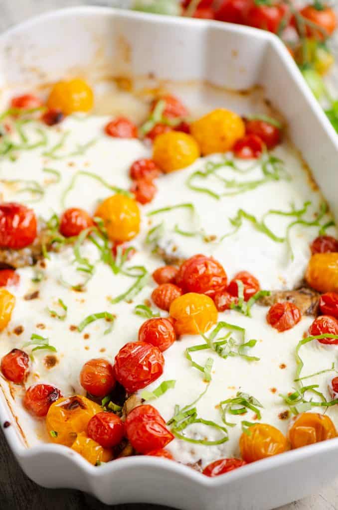 Honey Balsamic Caprese Chicken and tomatoes topped with basil in white baking dish