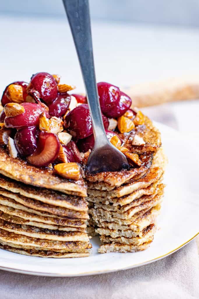 stack of Oatmeal Pancakes topped with cherry almonds and bite on fork